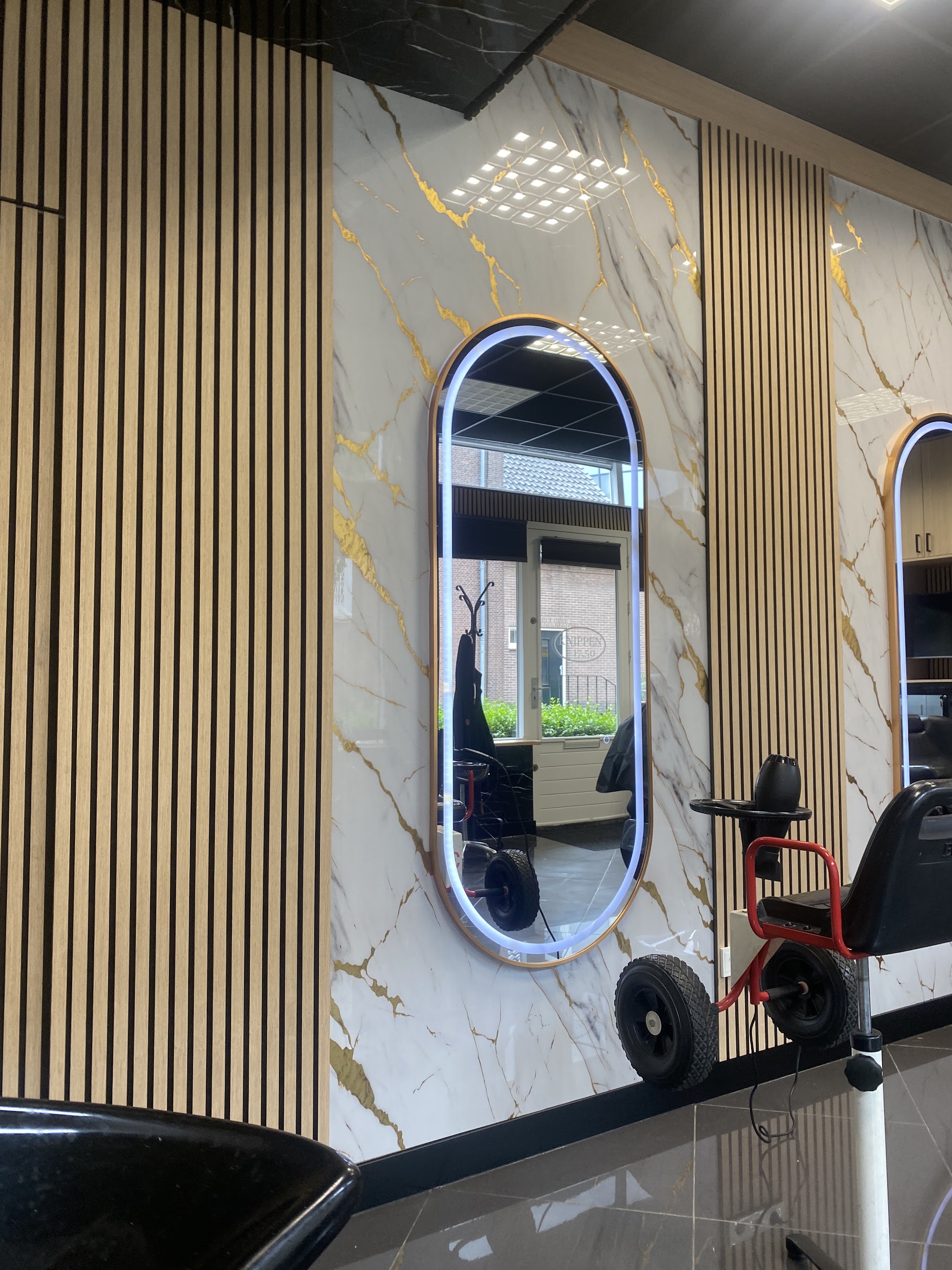 Een kappersplek met ovale spiegel en houten wandbekleding