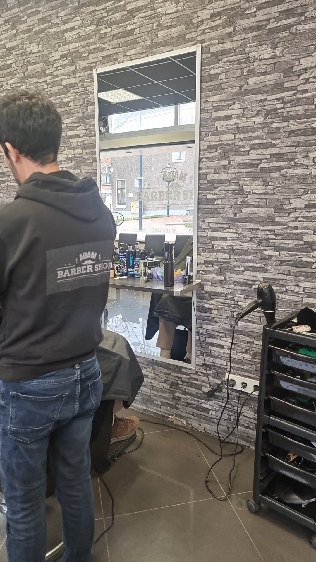 Een barbier van Adam barbershop aan het werk bij de spiegel